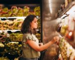 A woman selecting fresh vegetables from a supermarket aisle.